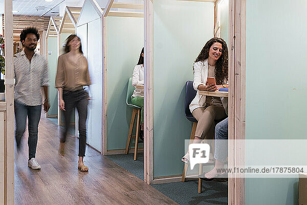 Businesswomen sitting in office cubicles with colleagues passing by