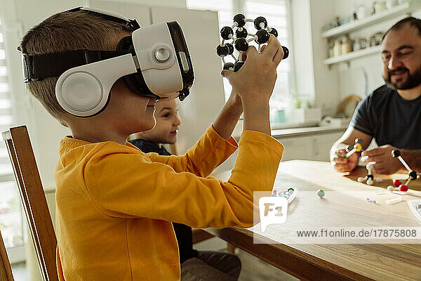 Boy wearing virtual reality goggles examining molecules at home