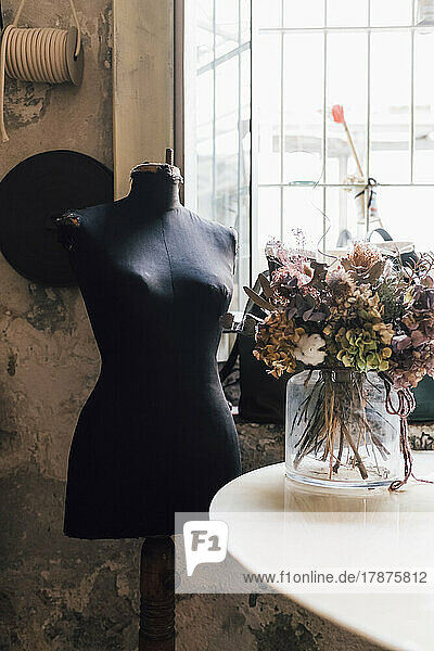 Dressmaker's mannequin by flower vase on table at workshop