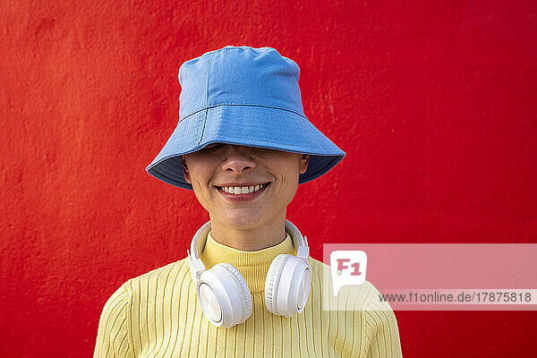 Smiling woman with headphones and blue bucket hat in front of red wall