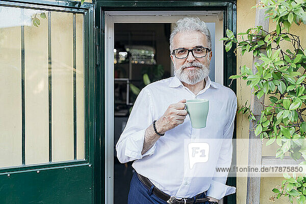 Senior businessman with coffee cup leaning at doorway