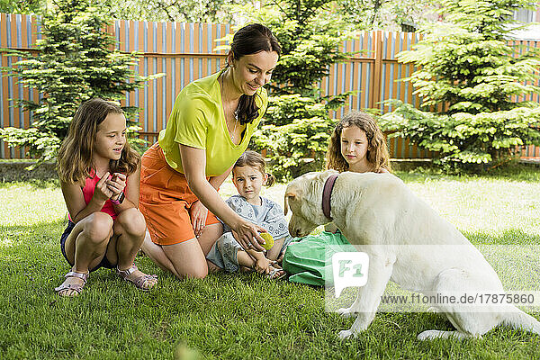 Smiling mother showing ball to dog by daughters at back yard