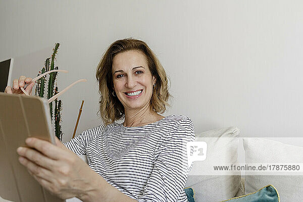 Smiling woman with tablet PC sitting on couch at home