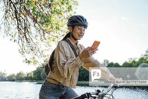Frau auf dem Fahrrad benutzt Mobiltelefon im Park