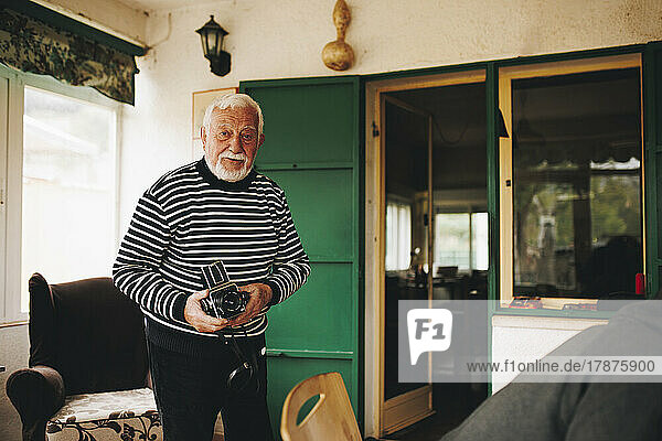 Älterer Mann steht mit Kamera zu Hause
