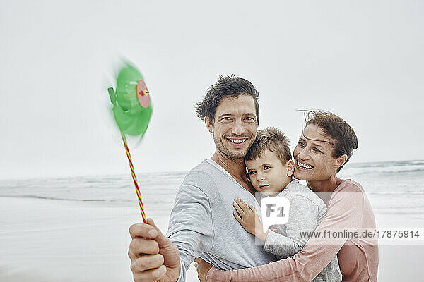 Glückliche Familie steht am windigen Strand und hält ein grünes Oinwheel in der Hand