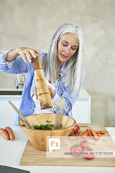Mature woman sprinkling pepper on vegetable in bowl