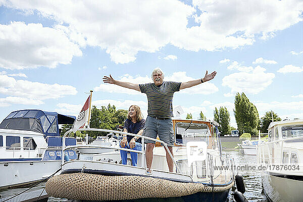 Senior man with arms outstretched standing on boat deck moored at harbor