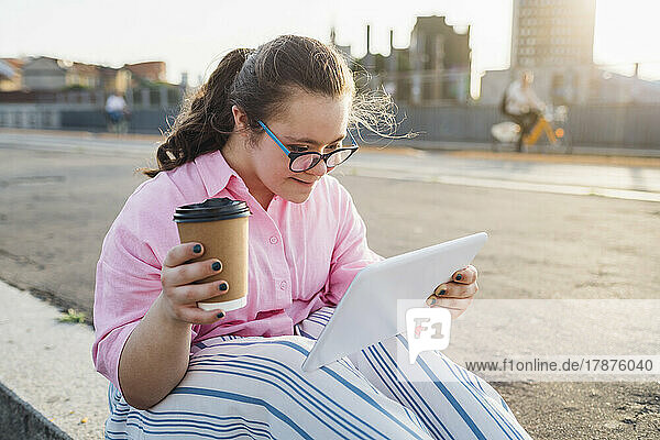 Teenage girl with disposable coffee cup using tablet PC by street