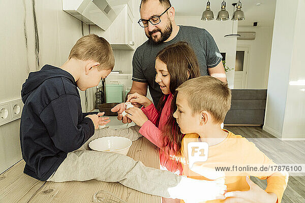 Children giving eggshells to father in kitchen