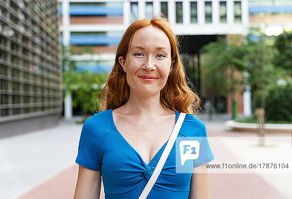 Smiling redhead woman by building in city
