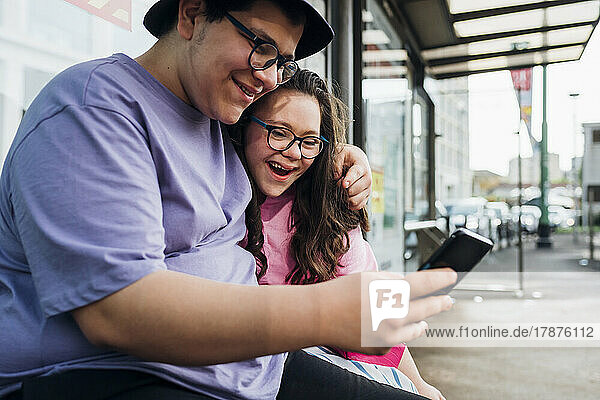 Smiling brother sharing smart phone with sister at bus station
