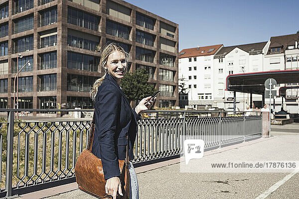 Happy blond woman with smart phone walking on road