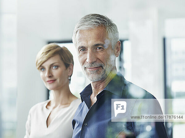 Smiling businessman with colleague seen through glass