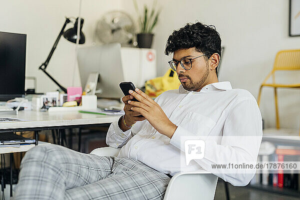 Young businessman using smart phone sitting at work place