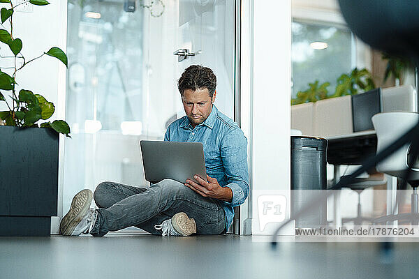 Businessman using laptop sitting on floor in office