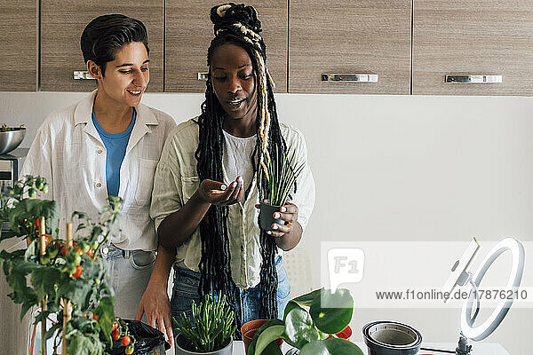 Smiling young woman with friend filming plant care tutorial at home