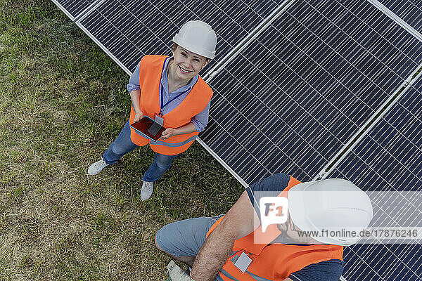 Happy woman with tablet PC standing by colleague at solar panel