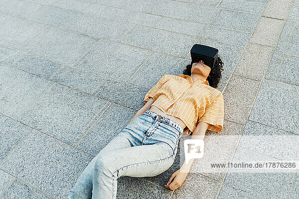 Woman with virtual reality headset lying down on footpath