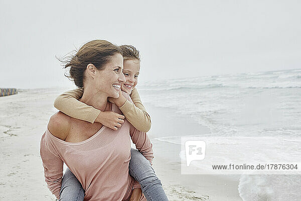 Mother walking on the beach carrying daughter piggyback