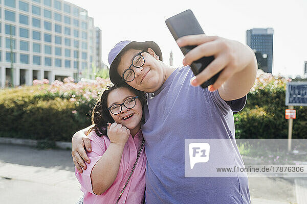 Smiling brother taking selfie with sister through mobile phone on sunny day