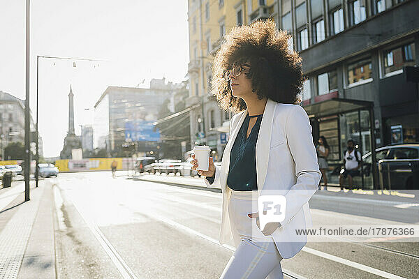 Junge Geschäftsfrau mit Kaffeetasse spaziert durch die Stadt