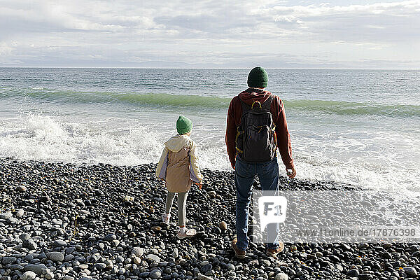 Father and daughter looking at sea standing on pebble beach