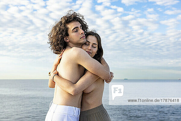 Romantic topless couple embracing by sea