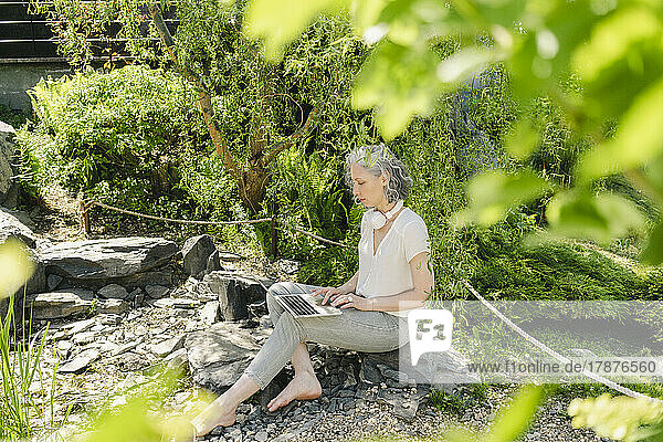 Freelancer working on laptop by plants in park