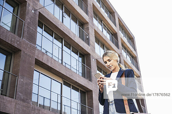 Smiling young woman using smart phone in front of building