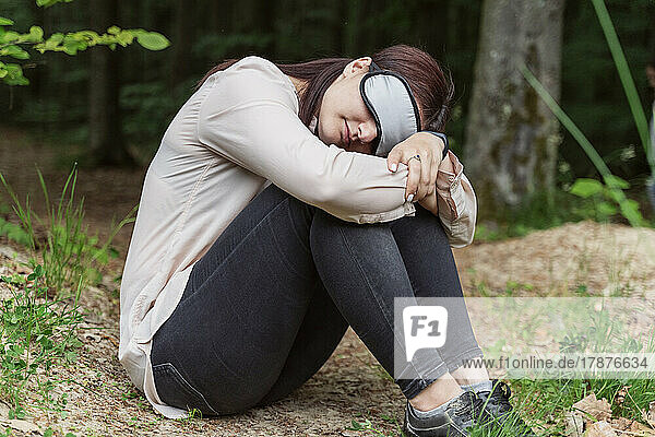 Woman wearing sleep mask sitting in forest