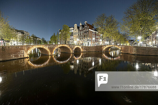 Niederlande  Nordholland  Amsterdam  beleuchtete Bogenbrücke  die sich nachts über den Stadtkanal erstreckt