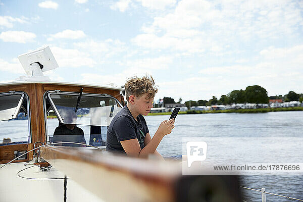 Boy using smart phone sitting on boat deck