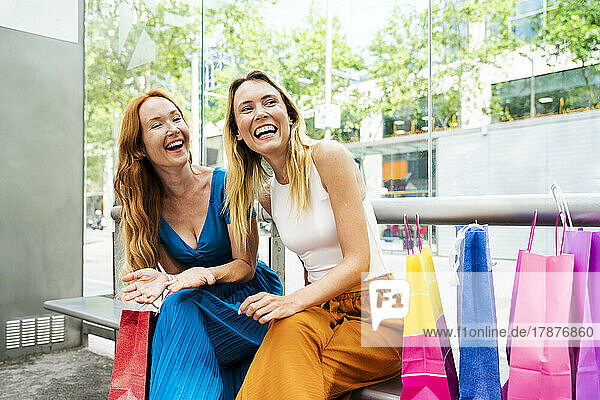 Happy friends with shopping bags at bench outside mall