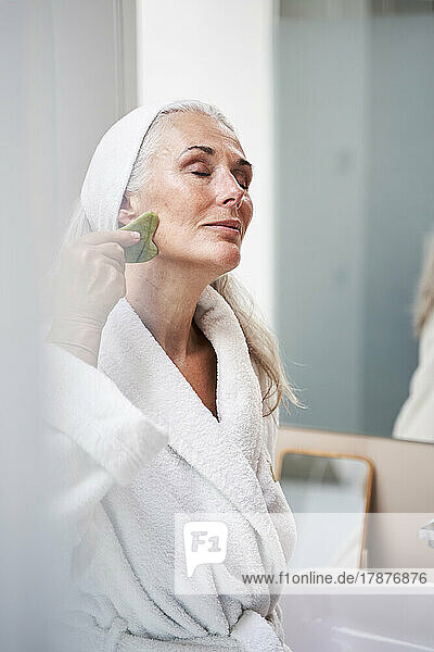 Beautiful woman massaging with jade stone in bathroom