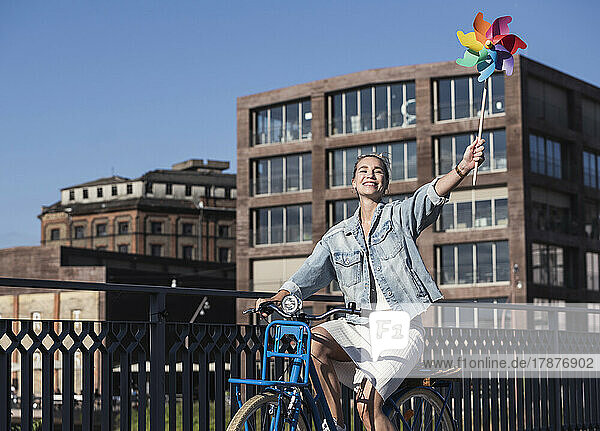 Happy woman with pinwheel toy riding bicycle on sunny day