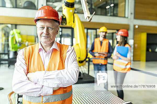Confident industrial worker standing in robotic factory with arms crossed
