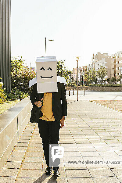 Businessman wearing box with smiley face walking on road