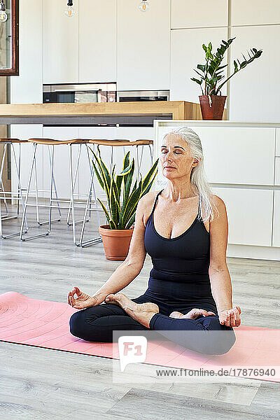 Fit mature woman with eyes closed sitting in lotus position at home