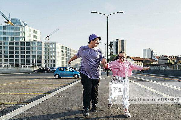 Happy brother and sister with down syndrome holding hands running on street