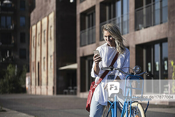 Happy young woman using mobile phone on bicycle