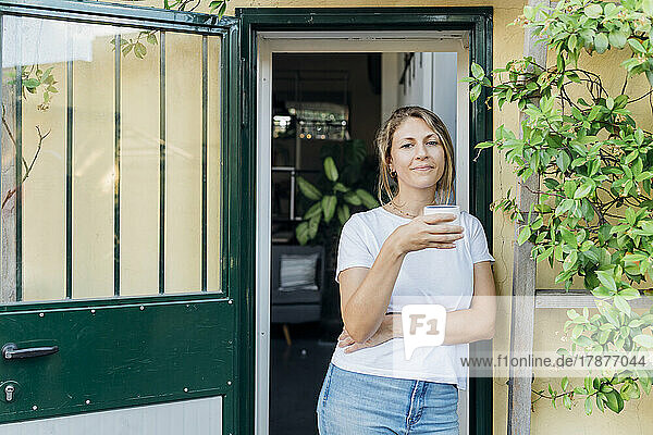 Businesswoman with coffee cup leaning at doorway