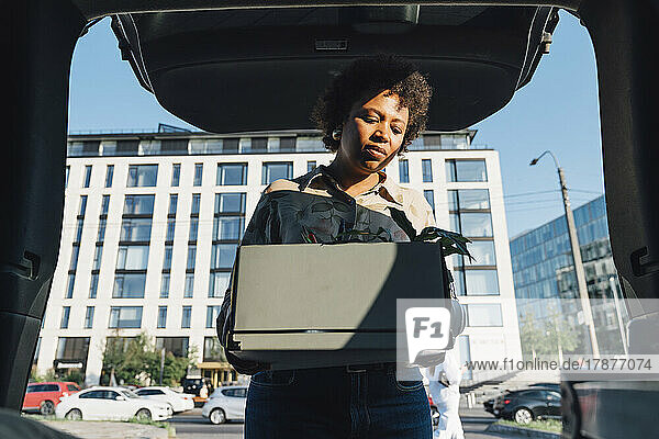 Businesswoman with curly hair keeping box in car trunk