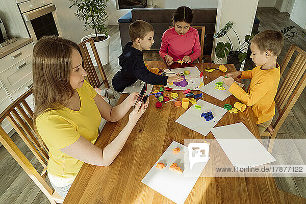Woman using smart phone by children playing with kinetic sand at home