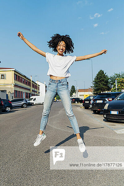 Happy woman with arms outstretched jumping on road