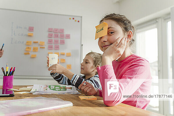 Mädchen mit Klebezettel auf der Stirn von Bruder beim Nachhilfeunterricht zu Hause