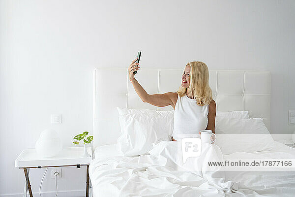 Woman taking selfie through mobile phone sitting on bed