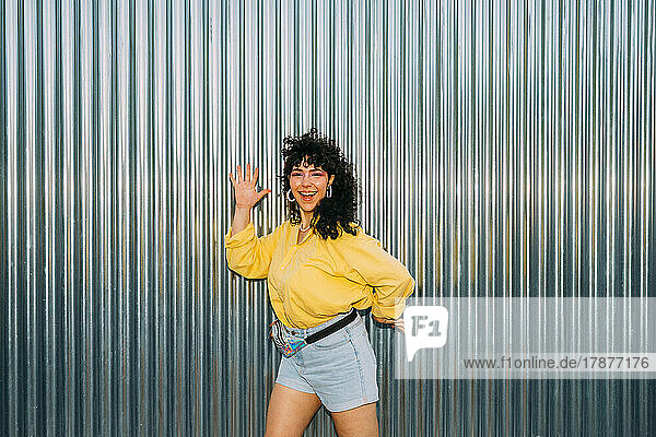 Happy woman gesturing and dancing in front of corrugated wall