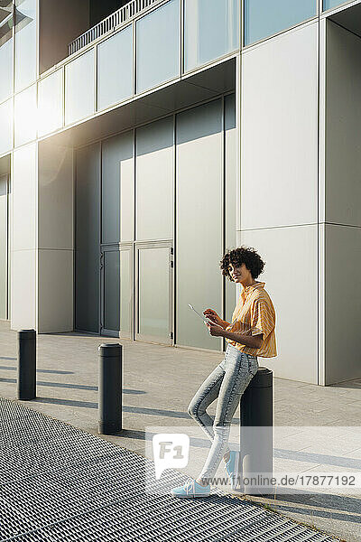 Freelancer with tablet PC leaning on bollard in front of building