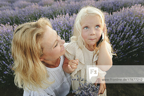 Happy woman with cute daughter talking on smart phone in lavender field